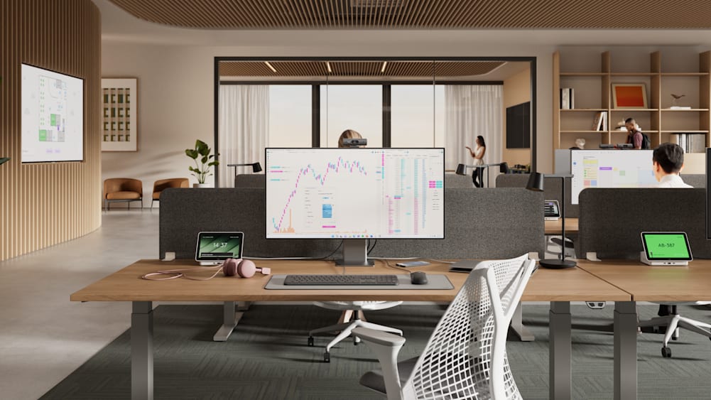 A modern, open-concept office space includes rows of flex desks, each with a monitor, Logi Dock Flex, and computer peripherals.