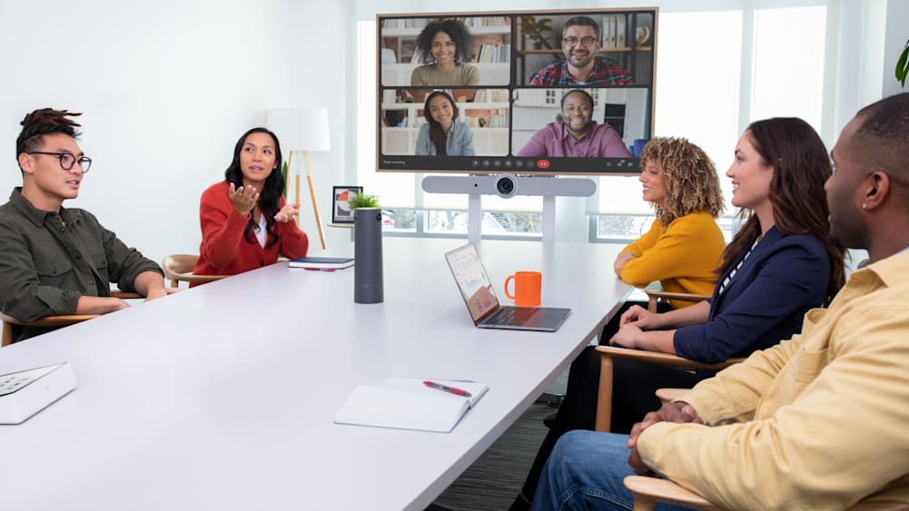 A team of five meets in a conference room to video conference with four colleagues using a Rally Bar and Logitech Sight.