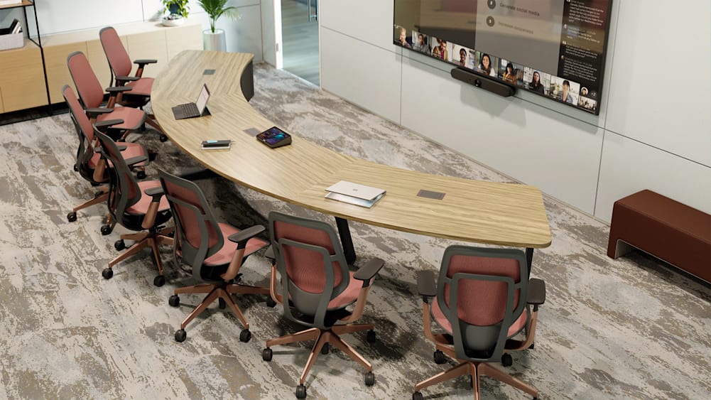 Modern conference room with a curved table, Logitech videoconferencing equipment, and a large screen displaying a video call.