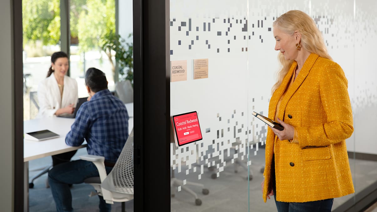A woman views Logitech Tap Scheduler as she walks by an occupied meeting room.