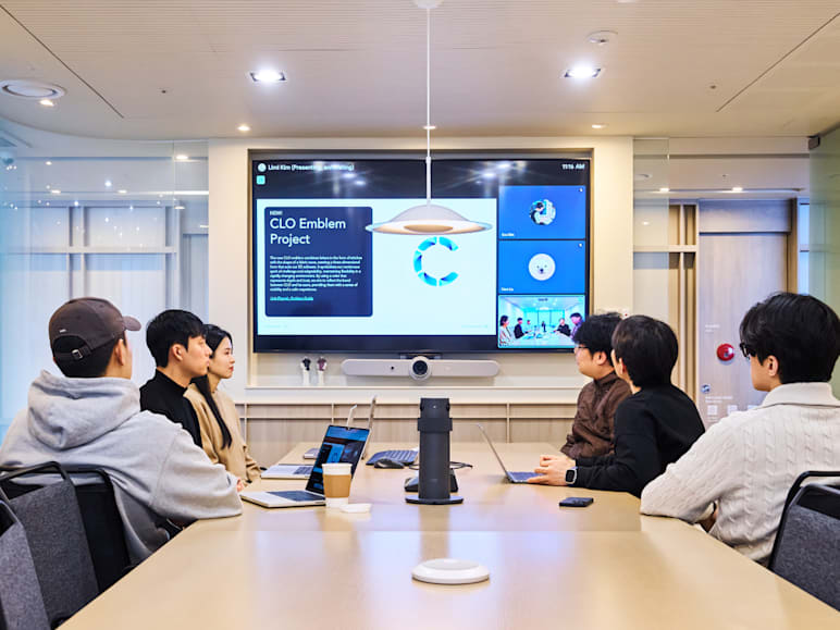 Team sitting at a meeting room table using Logitech Rally Bar, Sight, and Tap for video conferencing.
