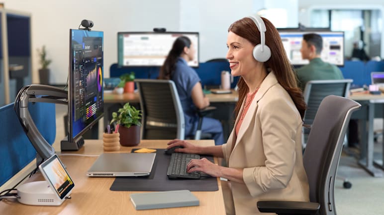 一名女性坐在办公桌前，戴着她的 Zone Wireless 2 ES for Business 耳机。