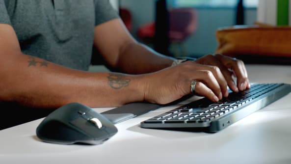 Pokazuje dłonie piszące na klawiaturze obok myszy biznesowych firmy logitech